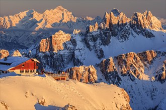 Mountain hut at sunset in the snow in front of rugged mountains, Rifugio Lagazuoi, Dolomites,