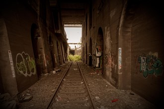 An abandoned railway tunnel with tracks lined with graffiti and rubbish, former Rethel railway