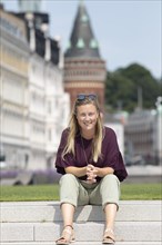 Swedish woman sitting on the steps in Angfaerjepark at the Kajpromenaden, portrait, behind the town