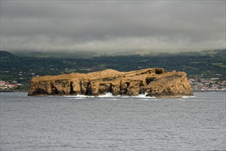 The remote rocky island 'Iieu Deitado' off a coastline of Pico under a cloudy sky, Iieu Deitado,