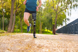 Legs of an unrecognizable man with prosthesis running along a park