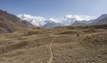 Hiking trail in the Achik Tash valley, behind glaciated and snow-covered mountain peak Lenin Peak