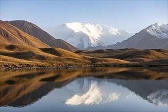 White glaciated and snowy mountain peak Pik Lenin at sunset, mountains reflected in a lake between