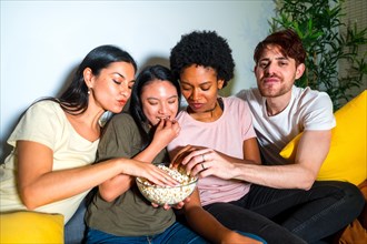 Friends enjoying popcorn during a movie night on the sofa at home