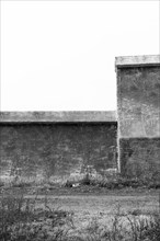 Black and white of small wire-frame and stucco building in countryside. Building has no window or