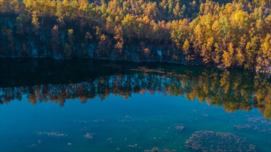 Autumnal forest with brightly coloured trees reflected in a calm lake, former Schlupkothen quarry,