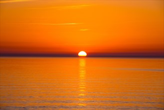 Intense, atmospheric sunset with bright orange-yellow sky over the Baltic Sea, reflection of the