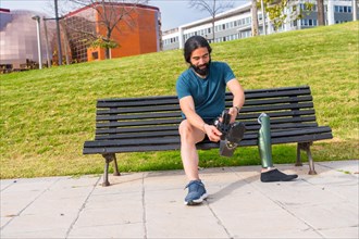 Physically disabled male runner adjusting prosthetic leg sitting on a bench in a park