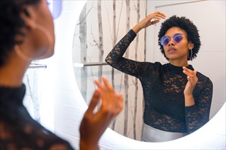African woman with sunglasses combing her hair getting ready for night party in front of mirror