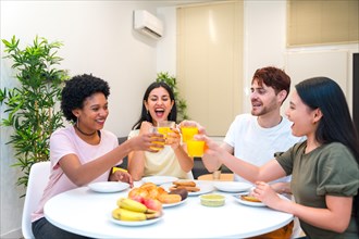 Multi-ethnic friends toasting with orange juice during breakfast at home in the morning