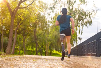 Rear view of a sportsperson with prosthetic leg running along a park