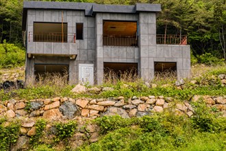 Unfinished abandoned gray concrete house in the side of a hill with stone wall in the foreground