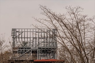 Metal frame of unfinished building abandoned in wooded countryside on an overcast day