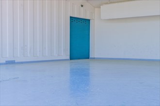 Large blue metal door in white wall reflecting onto concrete floor of amphitheater in urban public