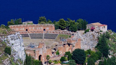 Remains of an ancient theatre on a cliff overlooking the sea under a clear blue sky, Taormina,
