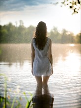 Suicidal thoughts, a young depressive woman with suicidal intent stands in the water by a lake in