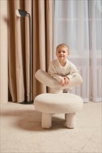 Cute little girl leaning on the back of a soft chair playing in the room