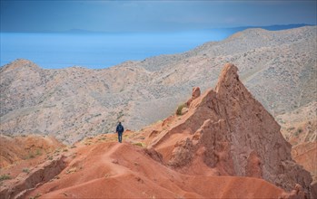 Hiker in front of eroded mountain landscape, sandstone cliffs, canyon with red and orange rock