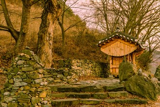 Small wooden oriental building with tiled roof in front of rock wall at rural roadside park on