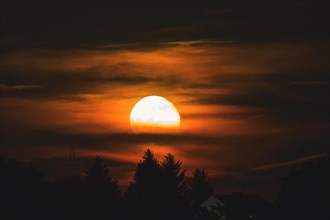 An atmospheric moonrise with orange glowing clouds and tree silhouettes, Haan, North