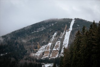 A ski jump tower stands on a snowy mountain slope with cloudy skies above, czech harrachov