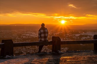 Person sitting on a wooden railing looking at the sunset over a wintry landscape, Wallberg,