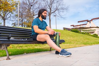 Adaptive male athlete adjusting his artificial running leg sitting on a park bench