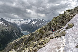 Mountaineer on hiking trail with snow, view of Schlegeisspeicher, glaciated rocky mountain peaks