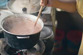Close-up of a hand stirring a pot of sikwate or Filipino hot chocolate drink in a traditional