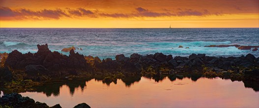 Panorama of the coastline at sunset with reflections on the water surface and a sailing boat in the