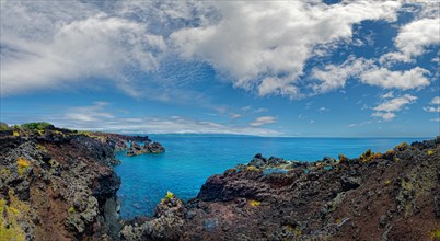 Dramatic view of a coastline lined with volcanic rocks under a clear sky, lava rocks coastal walk