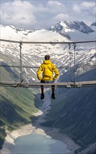 Mountaineer sitting on a suspension bridge, picturesque mountain landscape near the Olpererhuette,