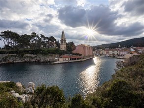 Sun breaking through clouds, view of the harbour entrance of Veli Losinj, with St. Anthony's