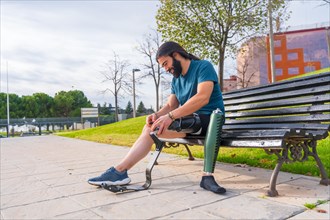 Amputee athlete adjusting his artificial running leg sitting on a park bench