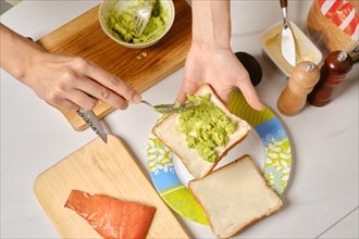 Top view of hands of woman spreading mashed avocado on toast