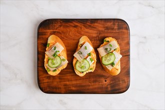 Top view of sandwiches with pieces of Clupeidae and spring onion on wooden serving board