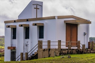 Side view of a small white country church sitting on a hillside in Guam with cloudy sky in the