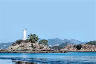 White lighthouse on small island at entrance to ocean harbor under clear sky