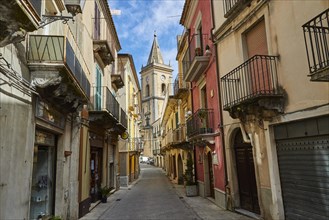 A narrow alley with colourful houses and a church tower at the end, Novara di Sicilia, Sicily,