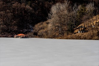 Winter landscape of oriental gazebo on shore of frozen lake where a fishing hut is docked