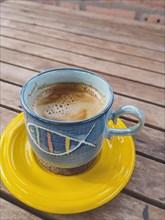 A cup of foamy, hot coffee on a wooden table, in a rustic ceramic cup