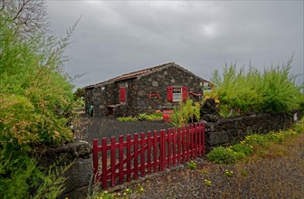 Stone house with red shutters and door and a red fence in a rural area, North Coast, Santa Luzia,