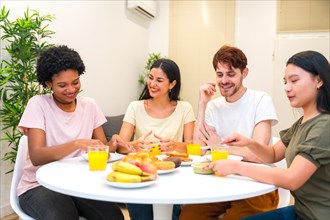 Multi-ethnic friends having healthy breakfast together at home sitting and sharing table