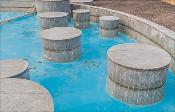 Large concrete cylinders inside dry fountain with bright blue bottom in public park