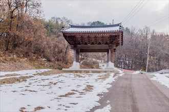 Wooden oriental gate beside rural mountain road on winter day under gray sky