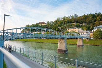 A long blue bridge over a river with green banks and blue sky, Mozartsteg, Salzburg, Austria,