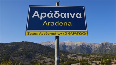 Town sign 'Aradena' with clear blue sky and mountain scenery in the background, Aradena Gorge,
