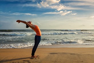 Young woman doing yoga Sun salutation Surya Namaskar pose Hasta Uttanasana on tropical beach on
