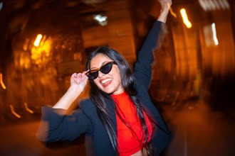 Night photo with flash and motion of a cool woman with sunglasses celebrating dancing in the city