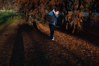 Male Golfer Below an Autumn Tree and Hitting His Golf Ball on Golf Course in Motion in a Sunny Day
